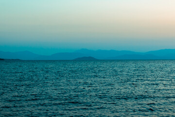 Surreal evening sea green and blue landscape, mountains on the background