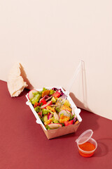 Creative concept of delivery restaurant authentic food.Healthy fresh vegetarian Fattoush salad in take away packaging box on red and beige background