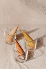 Various ice cream waffle cone in glass on beige pastel background. Summer creative concept