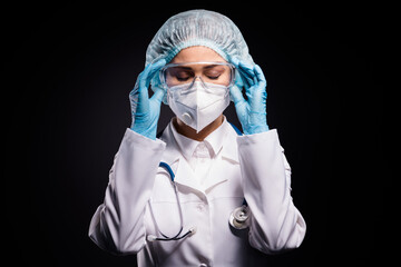 Fototapeta na wymiar Photo of tired lady doc hold arms on protective plastic goggles undressing after last late operation wear gloves mask coat facial glasses specs surgical cap isolated black color background