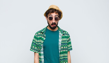young tourist man feeling terrified and shocked, with mouth wide open in surprise against white wall