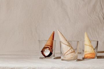 Various ice cream waffle cone in glass on beige pastel background. Summer creative concept