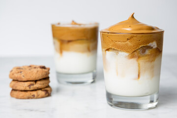 Two Dalgona coffee glasses with chocolate cookies on a marble table