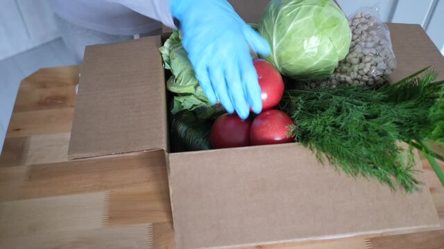 Volunteer in blue gloves holds food donation box vegetables to help others. donation package with foodstuffs. Video footage Full HD