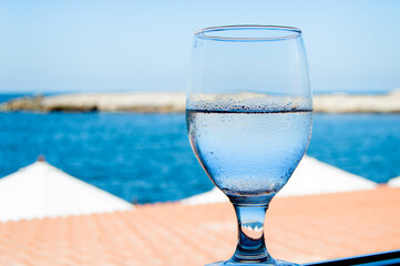 Cold glass of water by the Mediterranean sea with bokeh background on a hot summer day in an outdoor restaurant