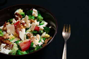 Close-up Broccoli Salad with Bacon, parmesan cheese in a black plate. In the right a silver fork. Healthy food concept