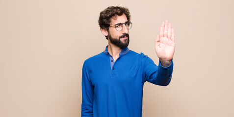 young handsome man looking serious, stern, displeased and angry showing open palm making stop...