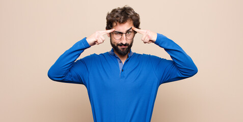 young handsome man with a serious and concentrated look, brainstorming and thinking about a challenging problem against flat wall