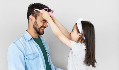 Obraz premium Portrait of lovely daughter smiling broadly puts the princess's crown on the head of her handsome father isolated over light gray background. Little girl and dad having fun on Father's Day.