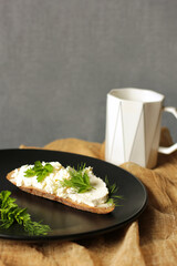 Sandwich with cottage cheese and herbs on a black plate. Homemade cottage cheese. Snack. Black utensils to use