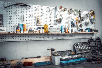 Moto workshop with hand mechanic tools kit. Workbench with sets of keys, screwdrivers, ploskobets, electrical tape, duct tape on wall. Table with motorcycle parts, vise. Workspace for auto mechanic