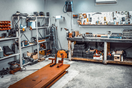 Garage, service area for disassembling, repairing motorcycles, car service station. Inside the workshop with large workbench, shelving, moto lift, tools kit for processing wrenches on the wall