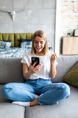 Excited woman watching media content on line in a mobile phone sitting on a couch in the living room at home