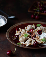 Dumplings with cherries and sour cream sauce on a plate, one cut, visible toppings.