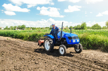 Obraz premium A farmer rides across the field on a tractor with a milling machine. Ground preparation for crop planting. Loosening surface, cultivating land for planting. Farming and agriculture. Work on the farm.