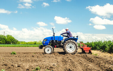 Obraz premium Farmer drives a tractor with a milling machine. Loosens, grind and mix soil on plantation field. Field preparation for new crop planting. Loosening surface, cultivating the land. Farming, agriculture.