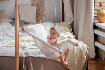 Adorable baby girl lying in a linen handmade swing. Scandinavian interior in modern apartment....
