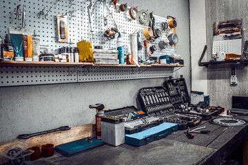 Inside the workshop. Large workbench and tools kit for working on the table close-up. Workspace for mechanic with wrenches, pliers on a metal wall. Garage for motorcycle repair, car service station. - obrazy, fototapety, plakaty