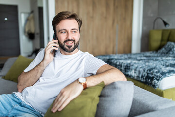 Portrait of cheerful man talking on the phone sitting at couch at home