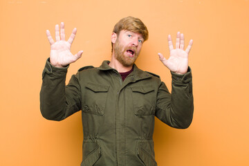 young blonde man feeling stupefied and scared, fearing something frightening, with hands open up...