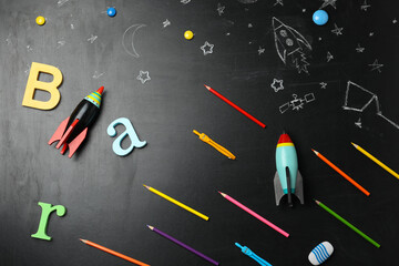 Bright toy rockets, school supplies and drawings on chalkboard, flat lay