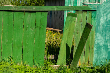 Green wooden fence with broken boards. Rural view.