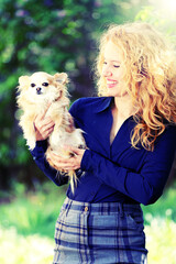 Blond young woman, business dressed, holding a long-haired chihuahua dog outdoor, on a green natural background ( with artistic filter )