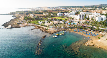 Fototapeta na wymiar Aerial bird's eye view of Pernera beach in Protaras, Paralimni, Famagusta, Cyprus. Tourist attraction golden sandy bay with sunbeds, water sports, hotels, restaurant, people swimming in sea from above