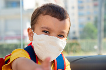 Little boy wearing white knitted cotton face mask as a protection against the novel coronavirus and...