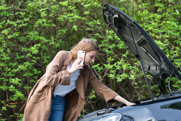 Helpless woman driver calling for help/assistance looking at broken down car, stopped at the roadside. Doesn't understand what happened.