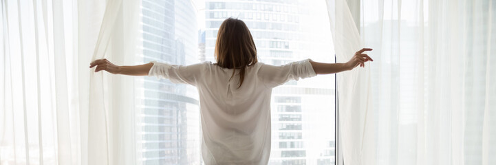 Rear back view woman opening white curtains enjoy cityscape modern skyscrapers buildings view and...