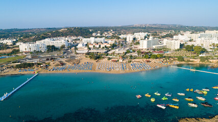 Aerial bird's eye view of Fig tree bay in Protaras, Paralimni, Famagusta, Cyprus. Famous tourist attraction golden sand family beach with boats, sunbeds, water sports pier, swimming in sea from above.