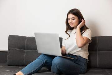 Fototapeta na wymiar young beautiful brunette woman working from home in her laptop sitting on the sofa in her appartment during quarantine isolation, stay safe home concept