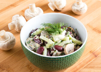 Tasty salad with beans, mushrooms and cucumber. Green bowl on a wooden background, no people