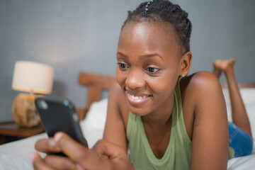 lifestyle home portrait of young happy and attractive black afro American woman lying on bed using social media app in mobile phone relaxed and cheerful online dating