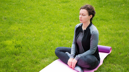 Naklejka na ściany i meble Yoga fitness caucasian woman wearing sportswear practicing yoga,closed eyes outdoor in park on green grass.Calm athlete meditating before strength training workout sitting in lotus position