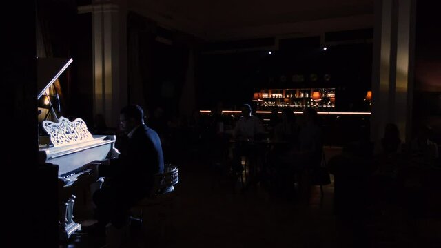 Wide shot of a pianist performing his own music on audience background. A classic and jazz music concert at night club.