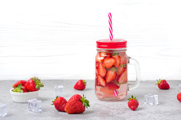 Strawberry infused water, cocktail, lemonade or tea. Summer iced cold drink with strawberry, leaf of mint, ice cube on white wooden background Flat lay