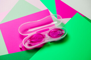 pink swimming glasses, with rubber strap on fuccia and green geometric background. Nobody, product concept