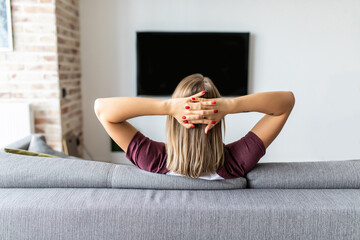 Back view of young woman sitting watching television program at home