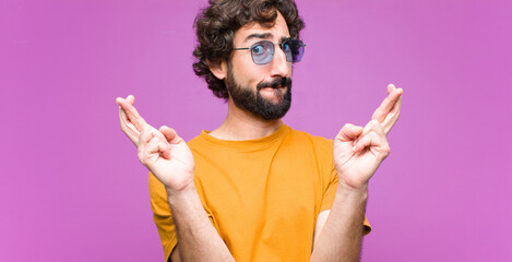 young crazy cool man crossing fingers anxiously and hoping for good luck with a worried look...