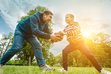 Father and son playing football, Father's day, Playful Man teaching Boy rugby outdoors in sunny day at public park. Family sports weekend.
