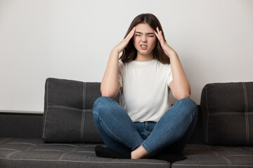 Obraz premium young beautiful brunette woman sitting on the sofa suffering from extreme headache looking desperate, healthcare and medical concept