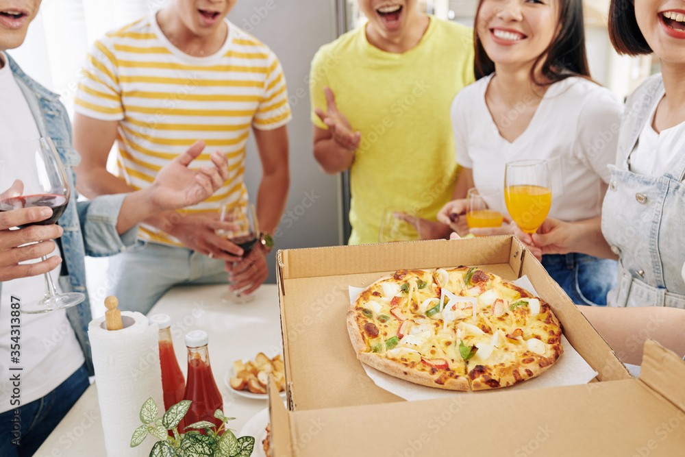 Poster party host opening box of delicious hot pizza in front of her excited friends