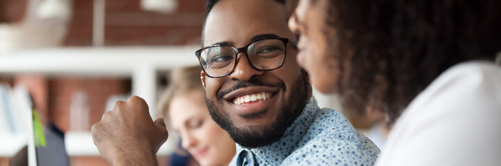 Diverse employees working in shared office focus on african guy flirting with female colleague,...