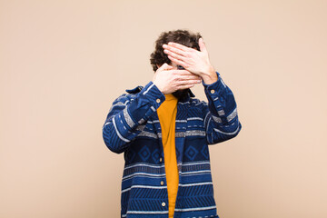 young crazy cool man covering face with both hands saying no to the camera! refusing pictures or...