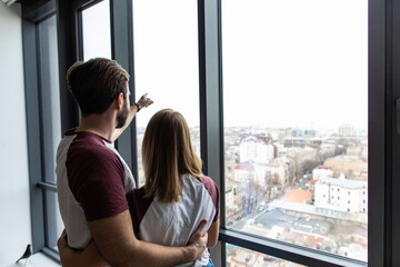 Rear view young couple embracing and pointing at something and look away to outside window