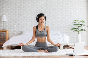Fototapeta na wymiar Asian indian woman wears headset yoga lotus pose online course at home