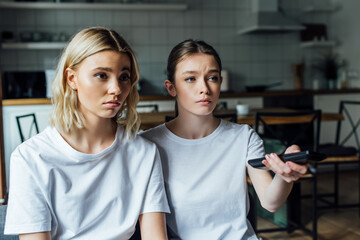 Sad girl sitting near sister while watching tv at home