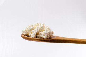 Closeup of wooden spoon full of tasty cottage cheese against bright background